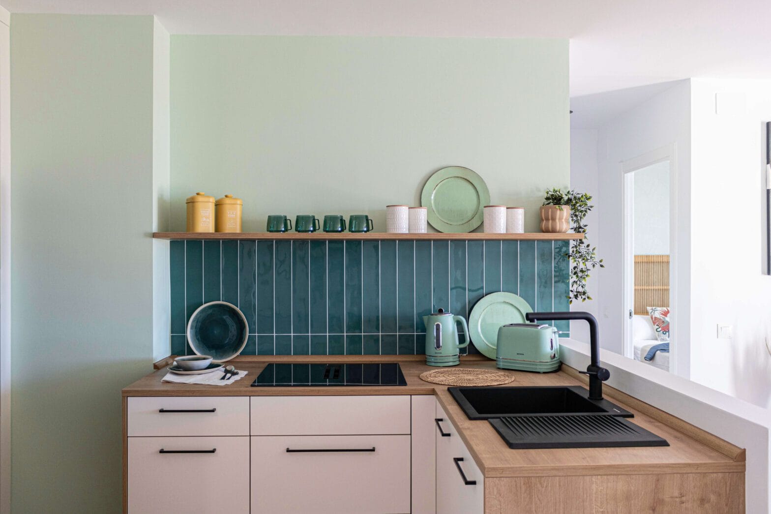Frente de cocina con azulejos en espiga verde menta, encimera blanca y detalles decorativos de madera en una reforma integral en Benalmádena.