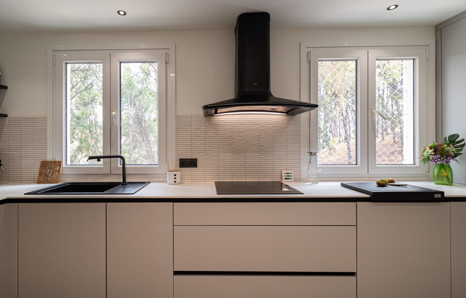 Diseño de interiores y reforma de cocina moderna en Málaga con mobiliario minimalista y campana decorativa negra.