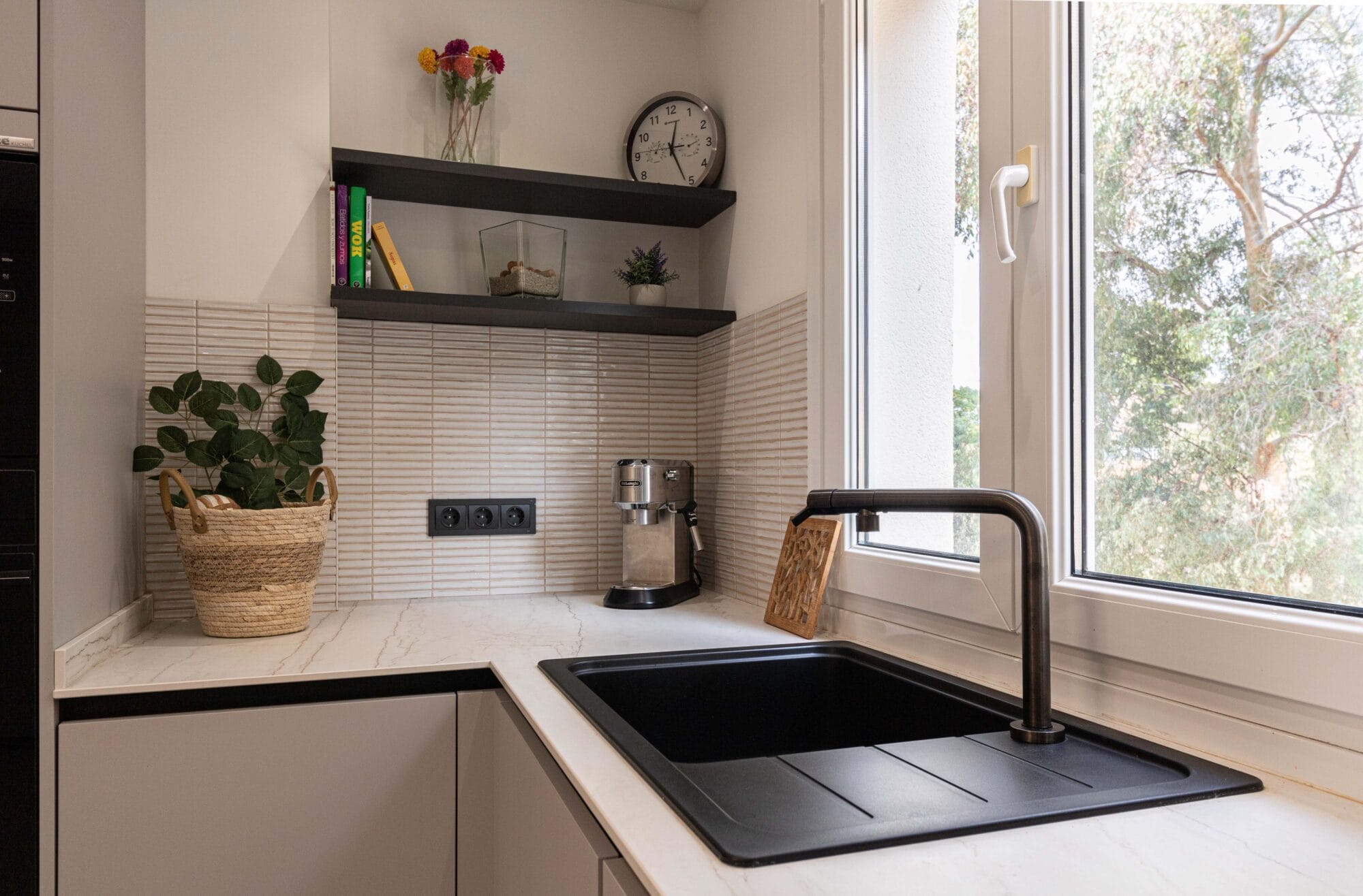 Decoración de interiores en Málaga, cocina con fregadero integrado negro con grifería moderna en cocina de diseño, estante flotante de madera con plantas y detalles decorativos.