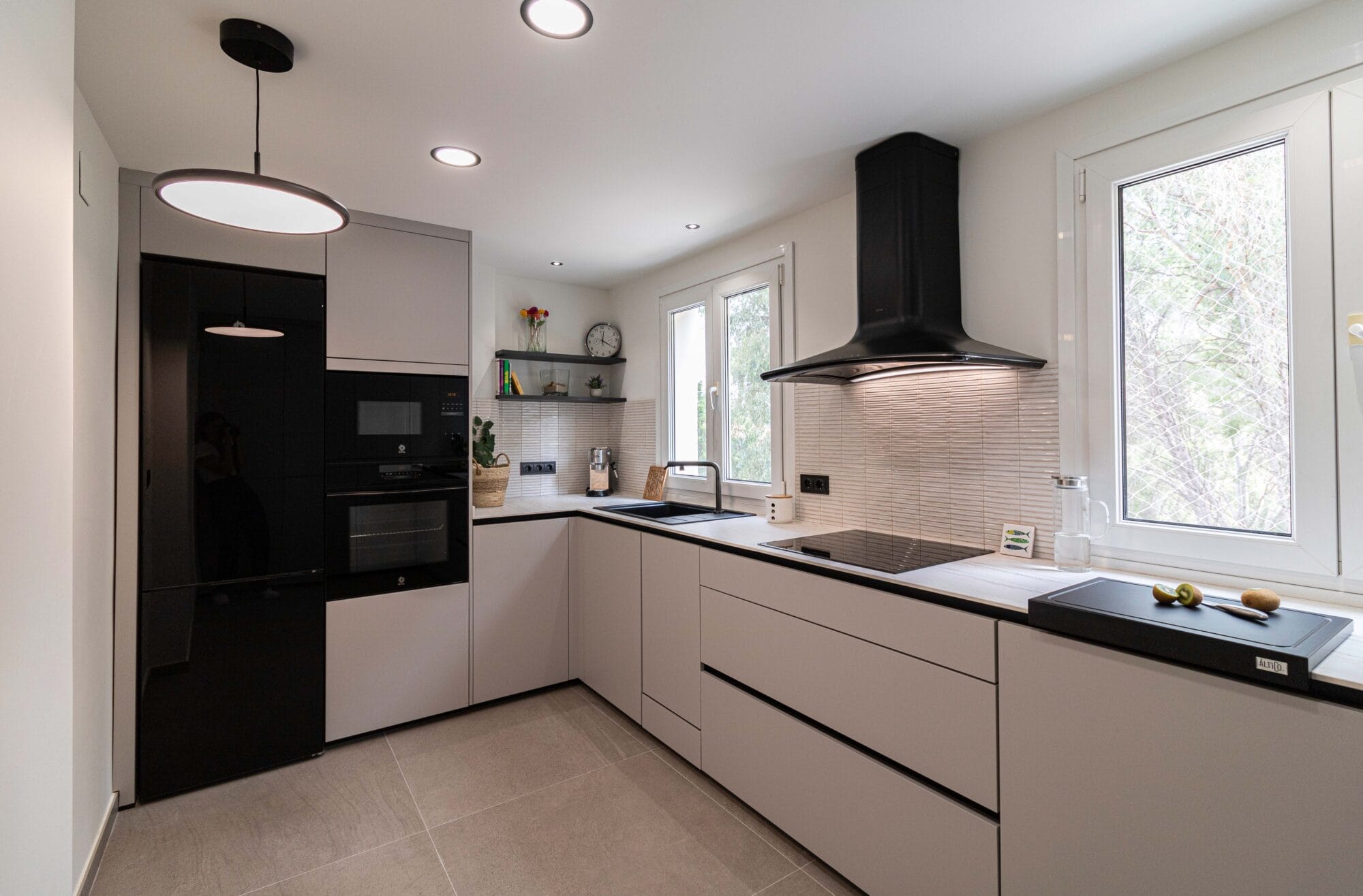 Interiorismo de cocina completa en forma de L, con electrodomésticos integrados negros, iluminación de diseño y distribución funcional.