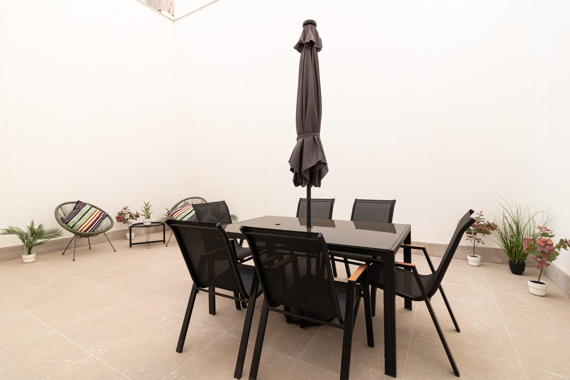 Amueblamiento y decoración de una terraza interior con un conjunto de mesa y sillas de exterior negras, sombrilla y plantas decorativas.