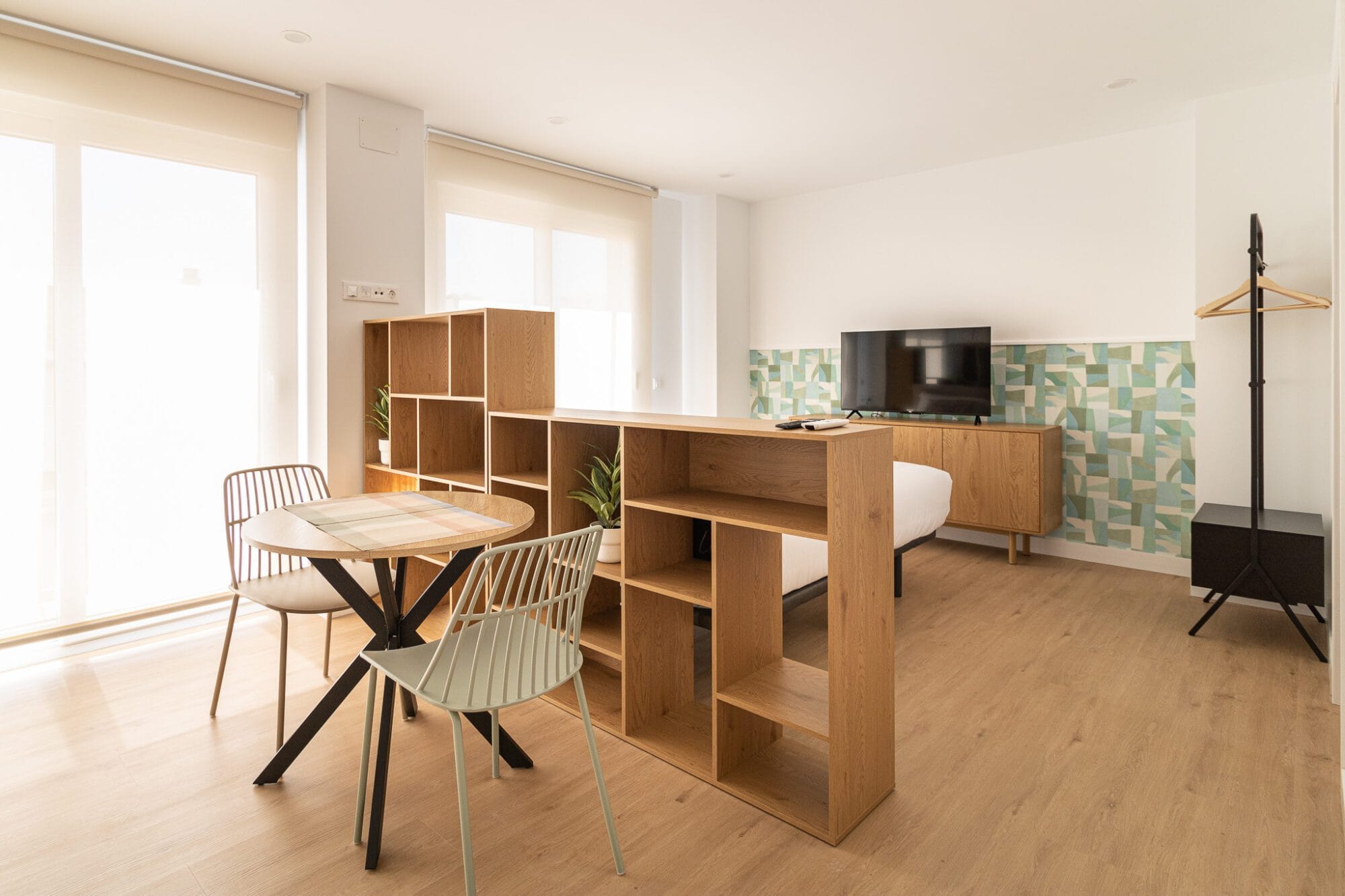 Decoración de un apartamento con una estantería de madera a media altura que separa de forma inteligente la zona de comedor del dormitorio.