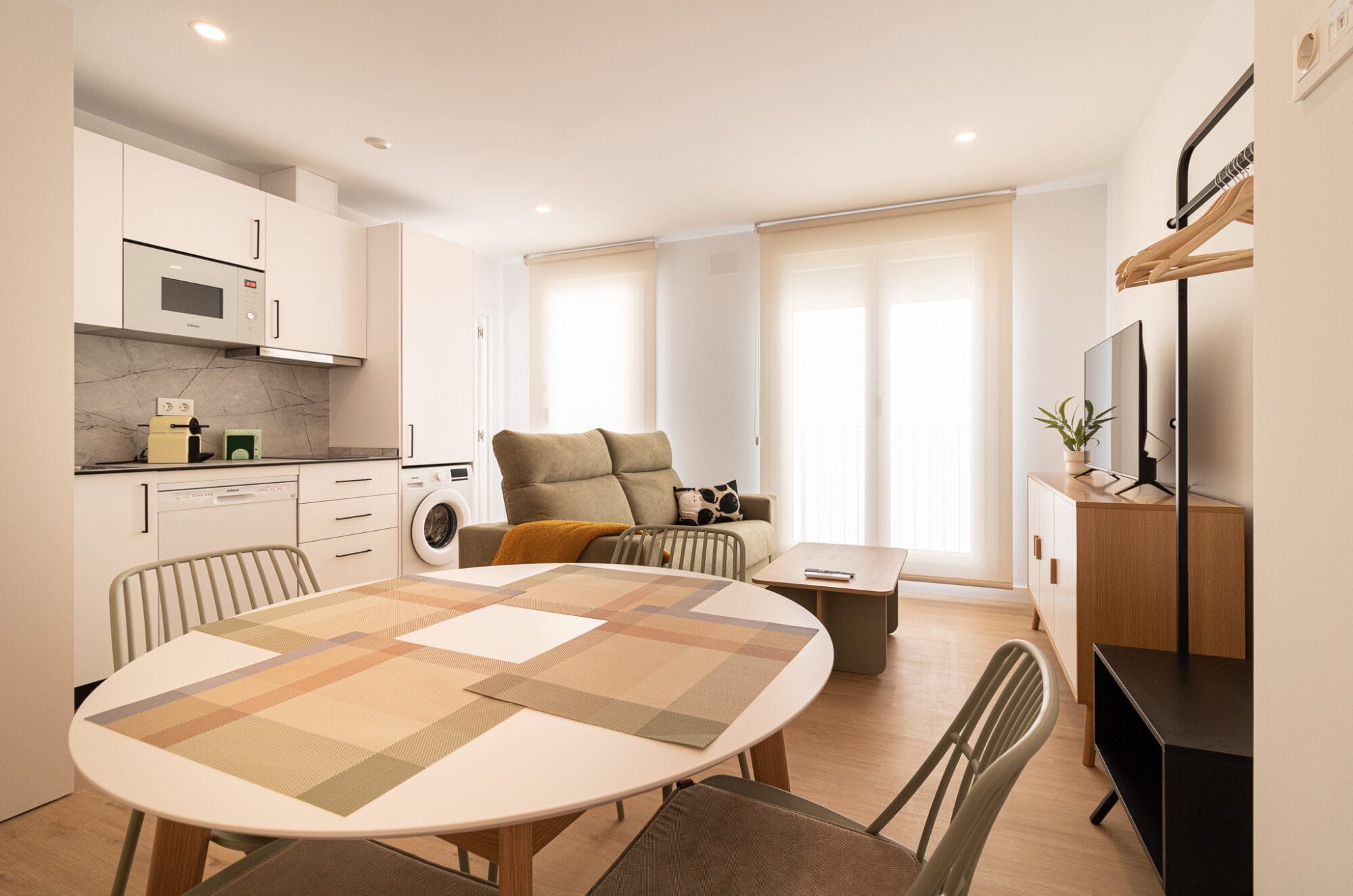 Reforma integral de un estudio de concepto abierto con una cocina compacta blanca, mesa de comedor redonda y un sofá al fondo.