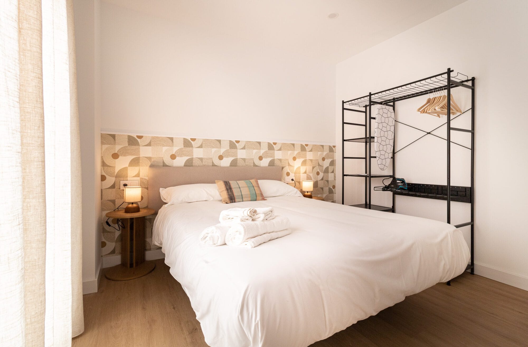 Dormitorio principal diseñado por un estudio de interiorismo en Málaga con papel pintado geométrico en tonos arena, textiles blancos y mobiliario minimalista.