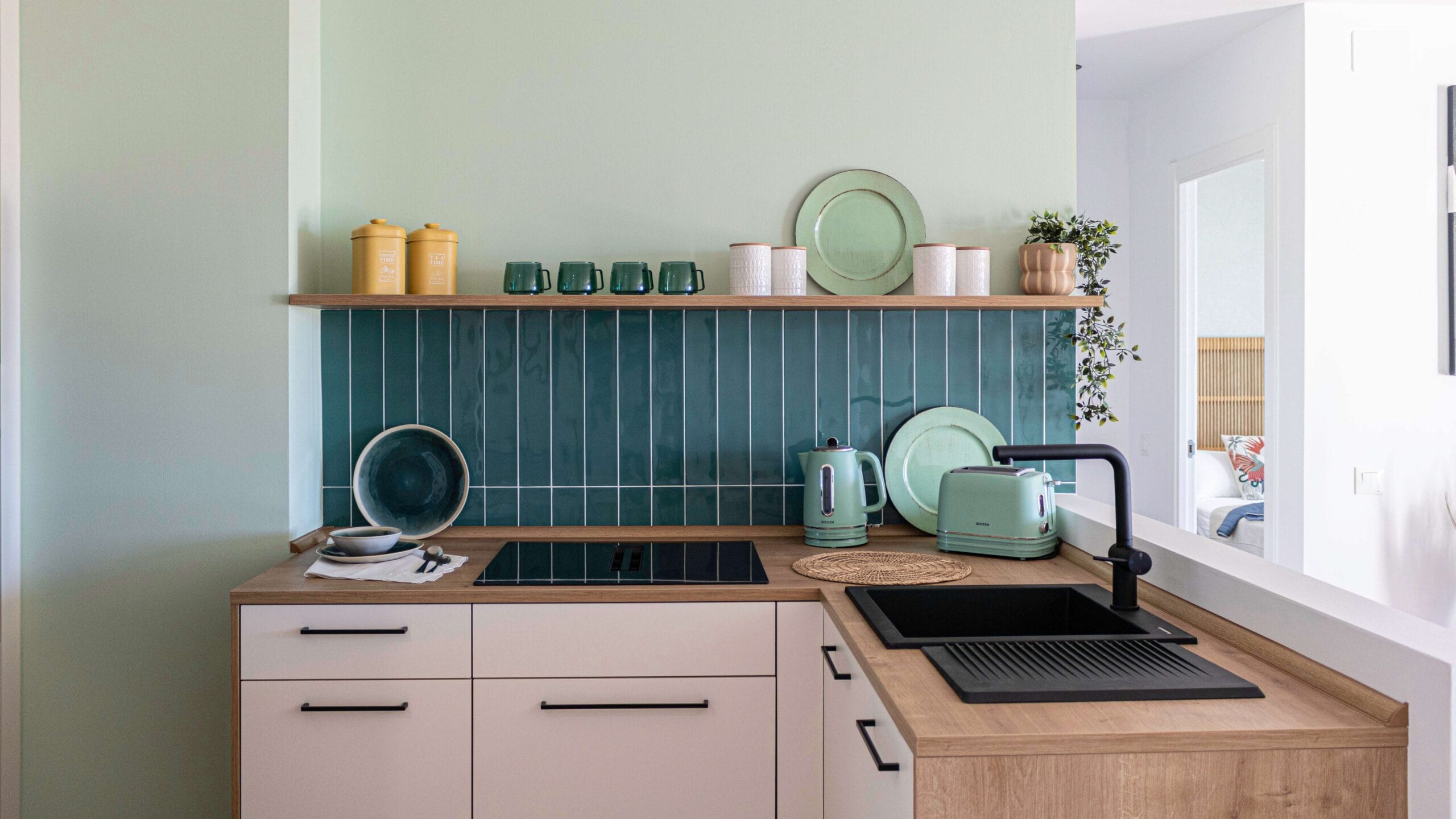 Frente de cocina con azulejos en espiga verde menta, encimera blanca y detalles decorativos de madera en una reforma integral en Benalmádena.